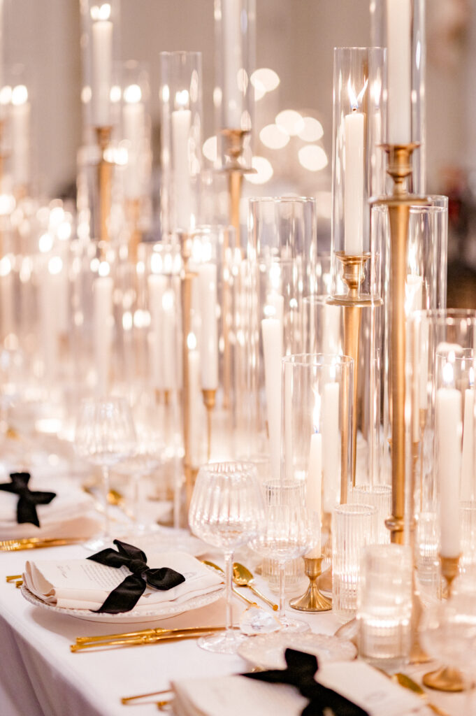 Close-up of glowing candlelight, crystal glassware, and black-ribboned menus on reception table, documenting fine details for a Newport wedding photography timeline by Jennifer Nichole.
